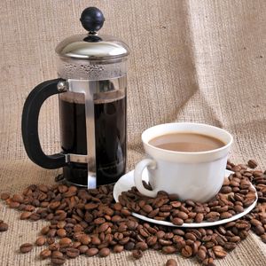 a french press full of coffee next to a mug of coffee and surrounded by whole coffee beans