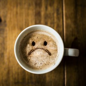 top view of a cup of coffee with a sad face drawn in milk froth