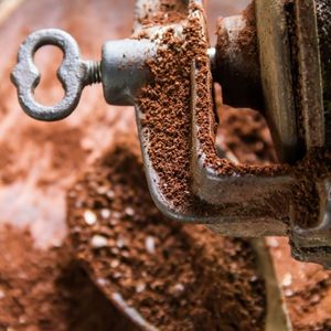 close-up view of a manual coffee grinder with coffee grounds spilling onto a spoon below it