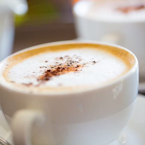 ceramic cup of coffee with thick foam and cinnamon or nutmeg on top